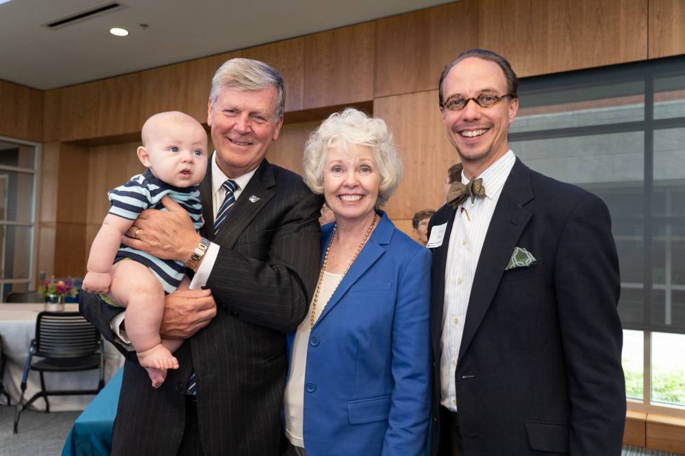 President Thomas J. Haas holding a baby with his wife Marcia Haas, and a guest at the Arend and Nancy Lubbers Student Services Center Dedication